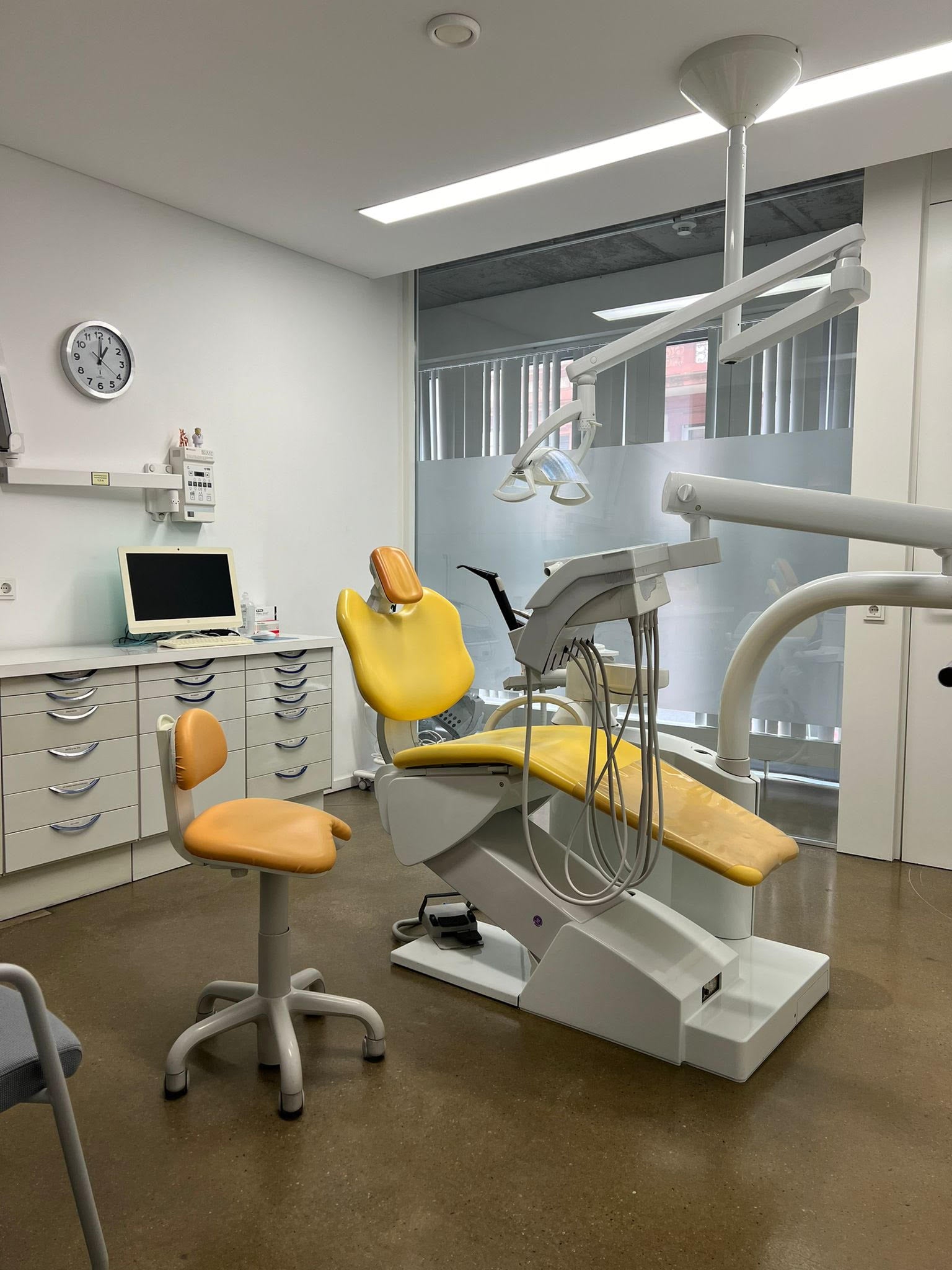 Zahnarzt Behandlungszimmer mit gelbem Stuhl in einem Raum abgetrennt durch eine Glasscheibe zum Flur